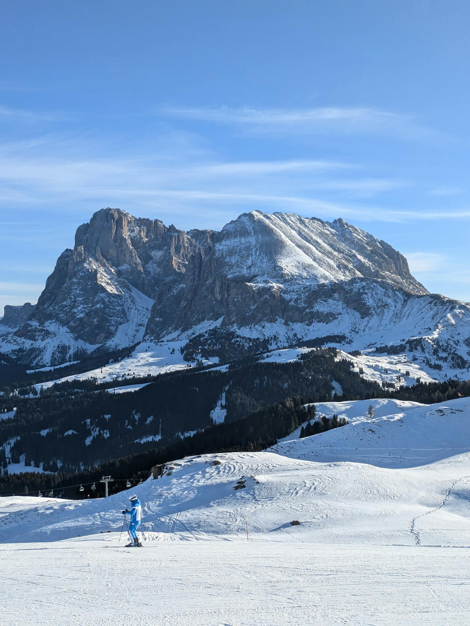 A skier in blue outfit enjoys a sunny day on the snowy slopes with stunning mountain views.